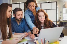 businesswoman-pointing-at-laptop-with-coworkers-at-desk-in-creative-office